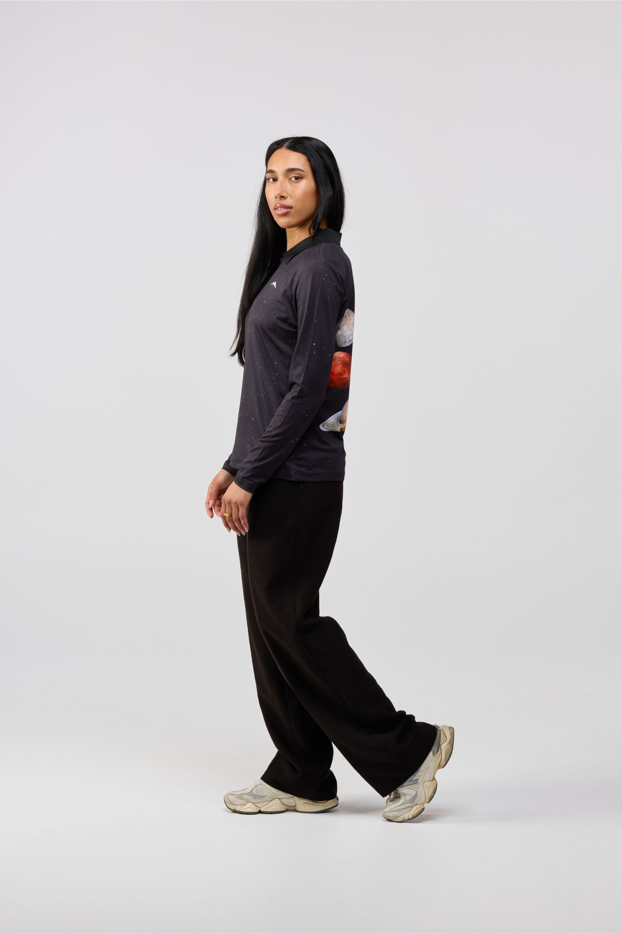 Person wearing a dark long-sleeve shirt with a graphic design and black pants on a white background